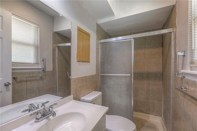 bathroom featuring tile walls, toilet, a shower stall, and vanity