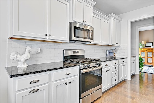 kitchen featuring light wood-type flooring, dark stone countertops, tasteful backsplash, white cabinetry, and appliances with stainless steel finishes