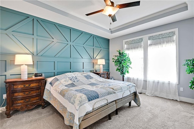 bedroom with crown molding, ceiling fan, light carpet, a decorative wall, and a raised ceiling