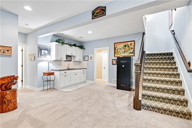 kitchen featuring a sink, decorative backsplash, light carpet, and white cabinets