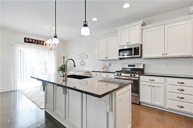 kitchen featuring wood finished floors, a sink, stainless steel appliances, white cabinetry, and tasteful backsplash