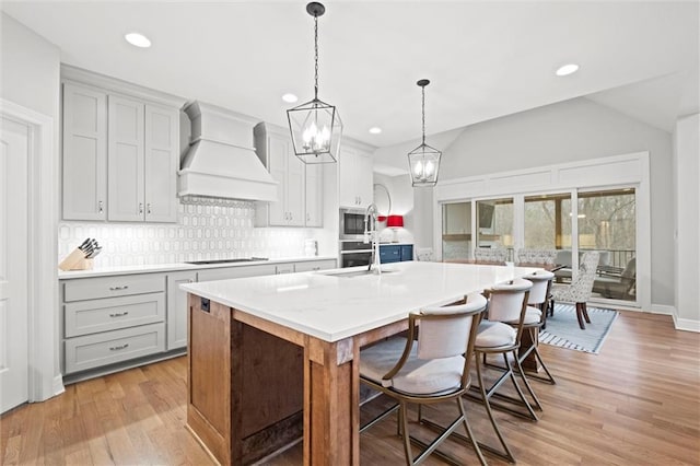 12745 N Larkspur Ln, Platte City, MO 64079 - kitchen with an island with sink, custom range hood, light countertops, stainless steel microwave, and backsplash