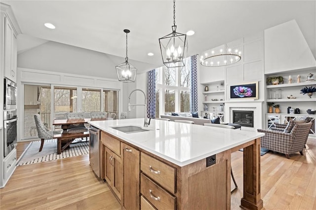 12745 N Larkspur Ln, Platte City, MO 64079 - kitchen featuring stainless steel appliances, a sink, light wood-style floors, a glass covered fireplace, and a notable chandelier