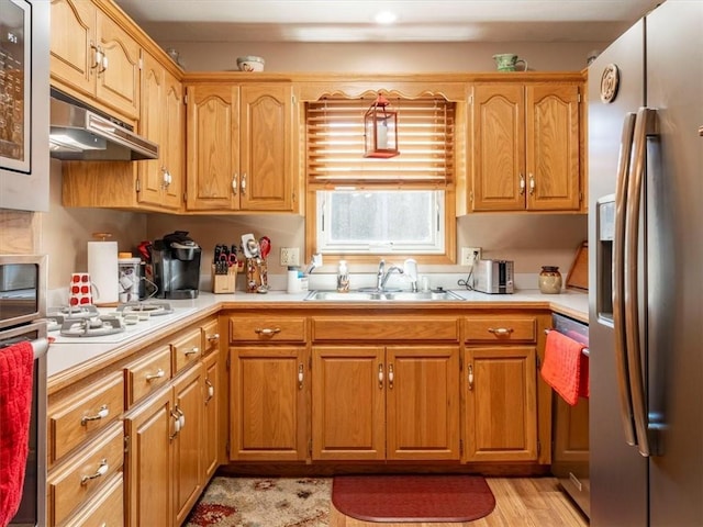 kitchen featuring under cabinet range hood, stainless steel appliances, light countertops, and a sink