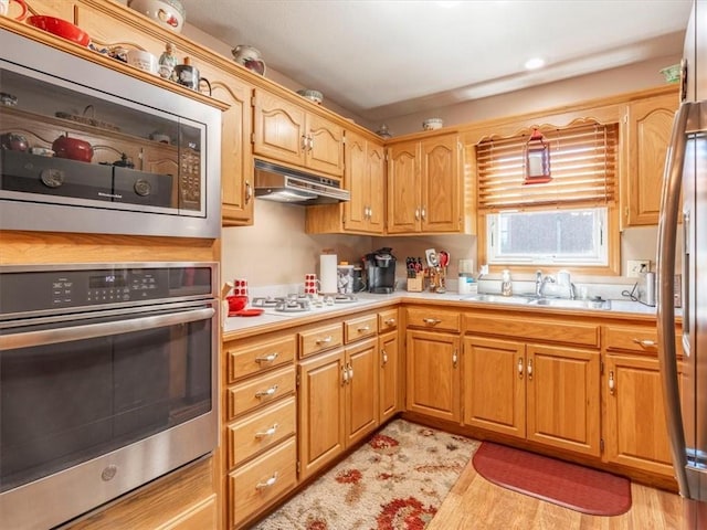 kitchen with under cabinet range hood, appliances with stainless steel finishes, light countertops, and a sink