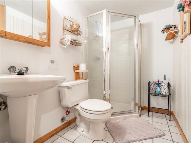 bathroom featuring tile patterned flooring, a shower stall, baseboards, toilet, and a sink