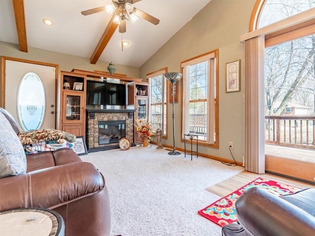 living area featuring a ceiling fan, carpet, baseboards, vaulted ceiling with beams, and a stone fireplace