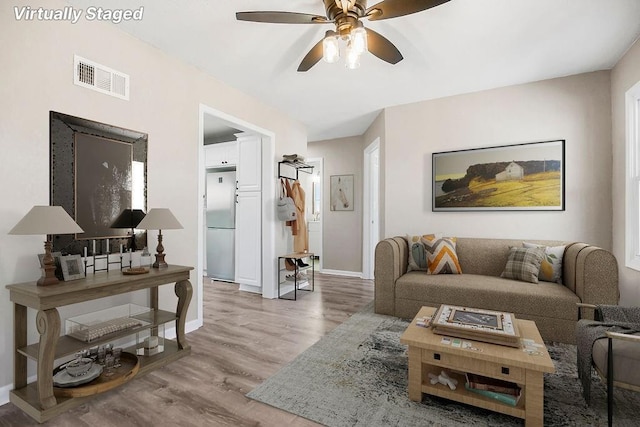 living room with visible vents, baseboards, ceiling fan, and light wood-style flooring