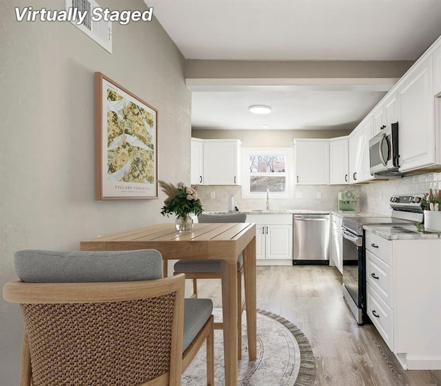 kitchen featuring a sink, stainless steel appliances, decorative backsplash, and light wood finished floors