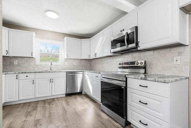 kitchen featuring tasteful backsplash, light stone counters, appliances with stainless steel finishes, light wood-style floors, and a sink