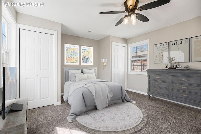 bedroom with dark carpet, a ceiling fan, baseboards, and two closets