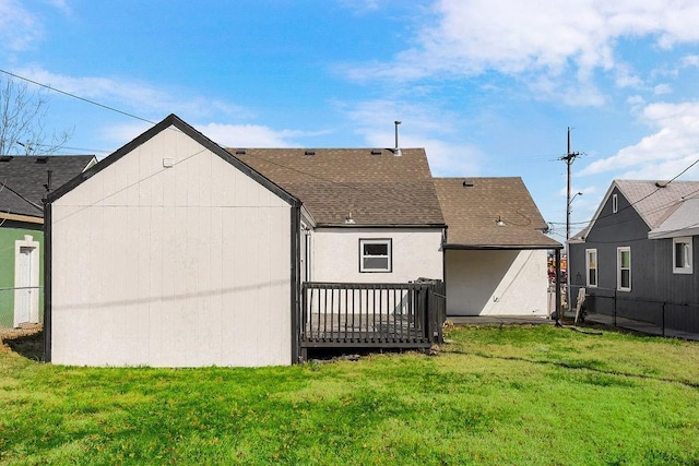 rear view of house with a lawn, a shingled roof, and a deck