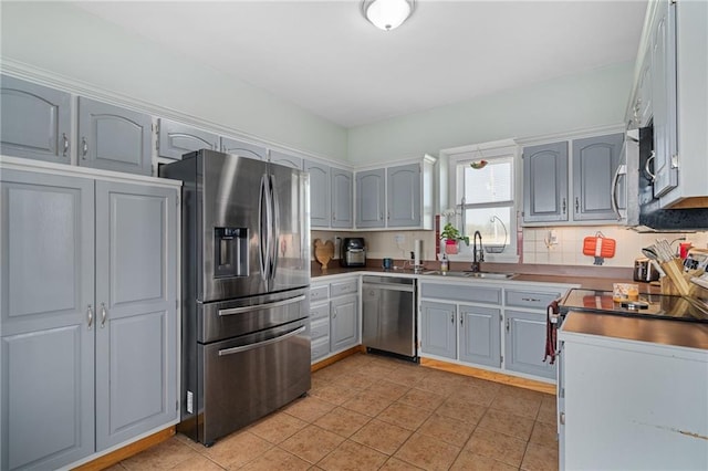 kitchen with gray cabinets, a sink, appliances with stainless steel finishes, light tile patterned flooring, and decorative backsplash