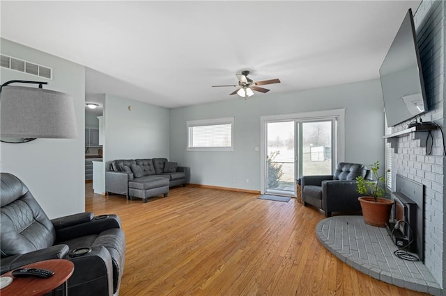 living area with baseboards, visible vents, light wood-style flooring, a fireplace, and ceiling fan