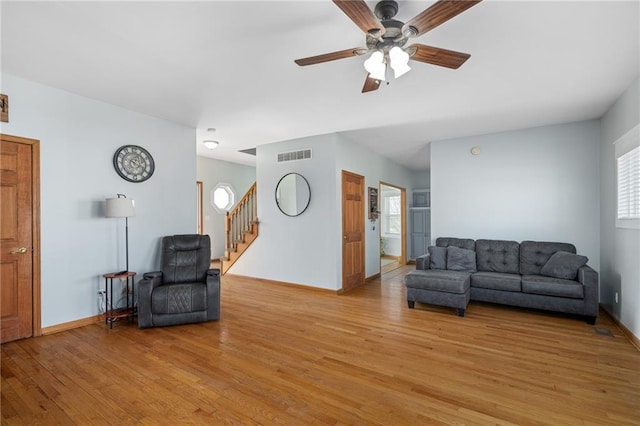 living area featuring visible vents, light wood-style flooring, baseboards, ceiling fan, and stairs