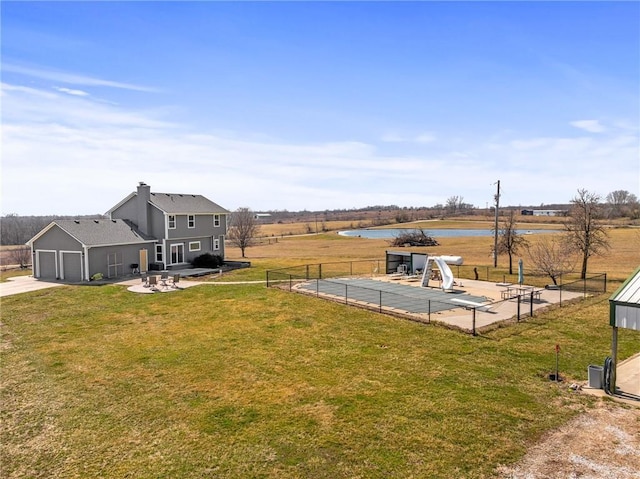 view of yard with a water view, driveway, a patio, fence, and an attached garage