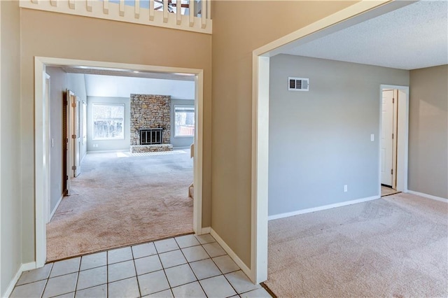 interior space with light tile patterned floors, baseboards, visible vents, a fireplace, and light carpet