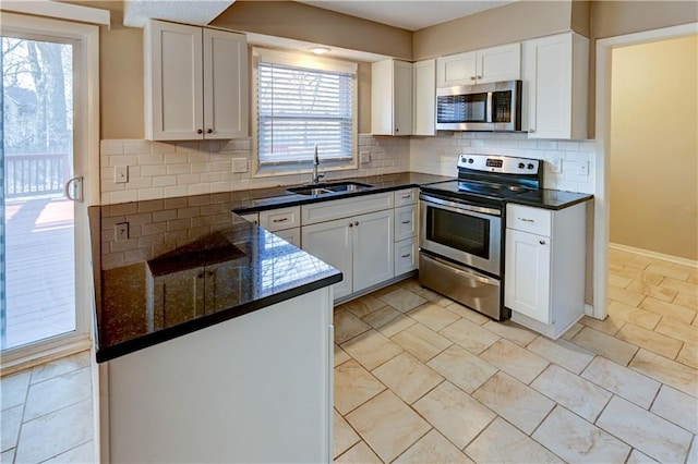 kitchen with a sink, backsplash, white cabinetry, appliances with stainless steel finishes, and baseboards