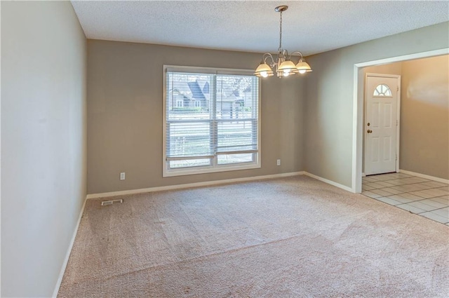 carpeted empty room featuring visible vents, a textured ceiling, an inviting chandelier, tile patterned flooring, and baseboards