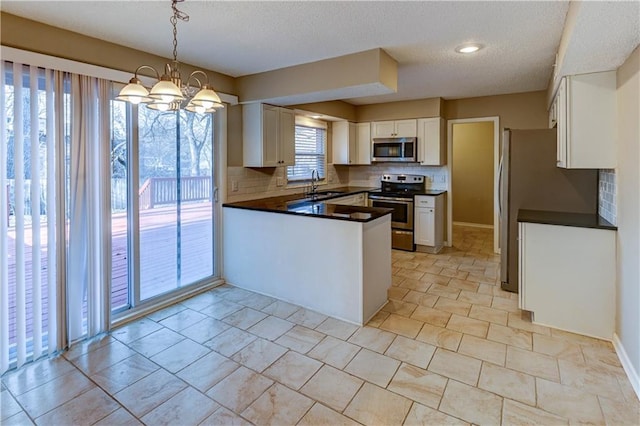 kitchen with a sink, dark countertops, appliances with stainless steel finishes, white cabinets, and a peninsula