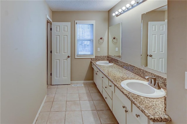 bathroom featuring tile patterned flooring, a textured ceiling, baseboards, and a sink