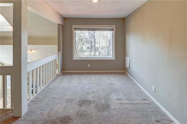 carpeted empty room with visible vents, a textured ceiling, and baseboards