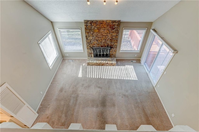 unfurnished living room with visible vents, a textured ceiling, a stone fireplace, and carpet flooring