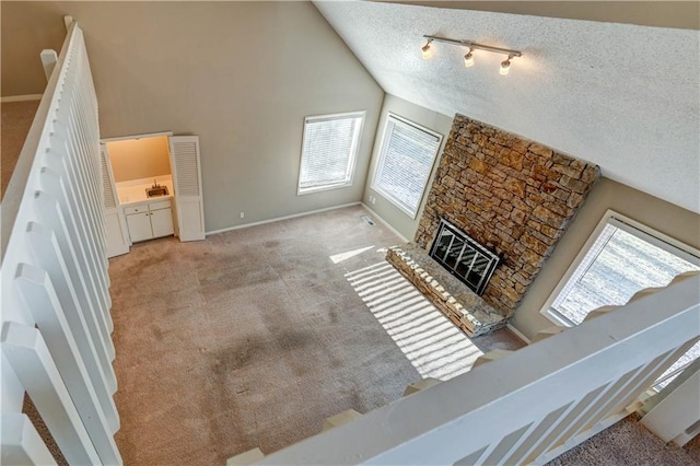 carpeted living room with baseboards, high vaulted ceiling, a fireplace, track lighting, and a textured ceiling