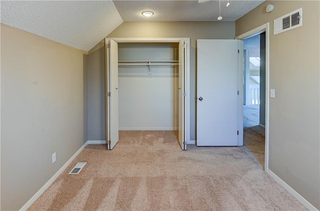 unfurnished bedroom featuring a closet, visible vents, a textured ceiling, and carpet floors