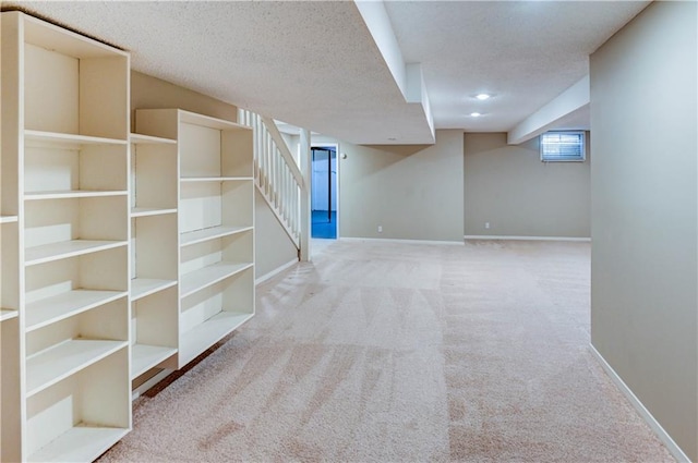 basement featuring stairway, baseboards, carpet floors, and a textured ceiling