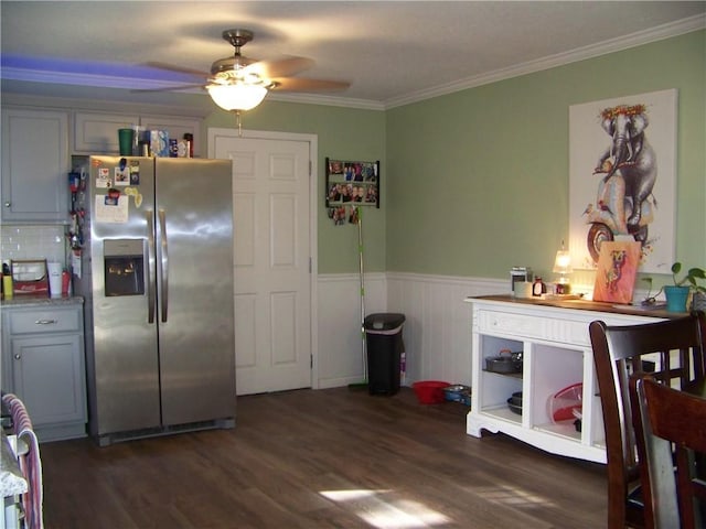 kitchen with crown molding, a wainscoted wall, stainless steel refrigerator with ice dispenser, a ceiling fan, and dark wood-style flooring