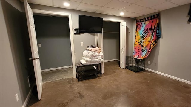 unfurnished bedroom featuring a drop ceiling, unfinished concrete flooring, and baseboards