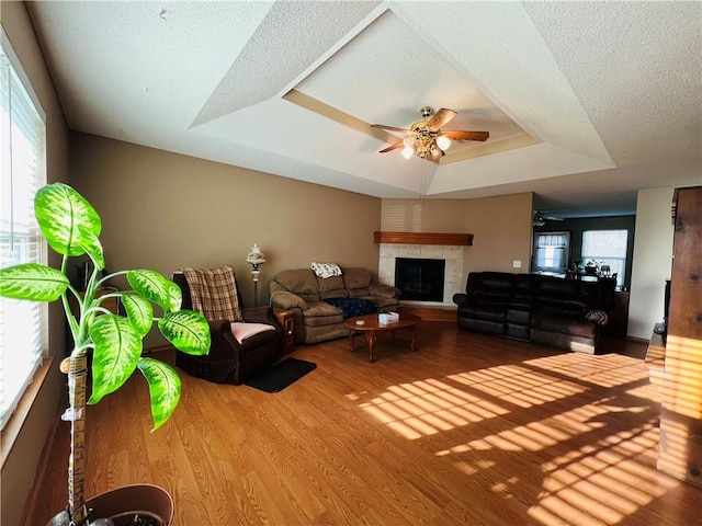 living area with plenty of natural light, ceiling fan, a tray ceiling, and wood finished floors