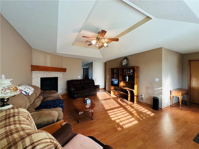 living room featuring a tiled fireplace, a tray ceiling, a textured ceiling, wood finished floors, and ceiling fan