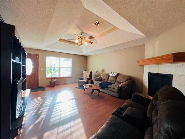 living area with visible vents, ceiling fan, a fireplace, wood finished floors, and a raised ceiling