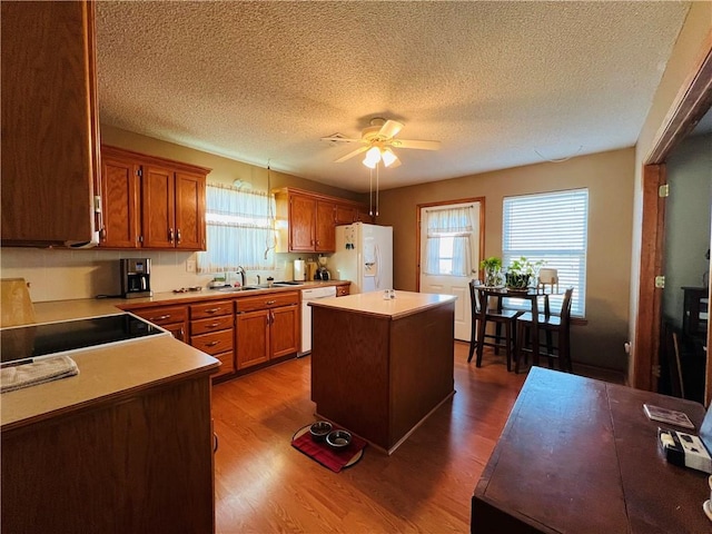 kitchen featuring a kitchen island, dark wood-style floors, white appliances, a ceiling fan, and a sink