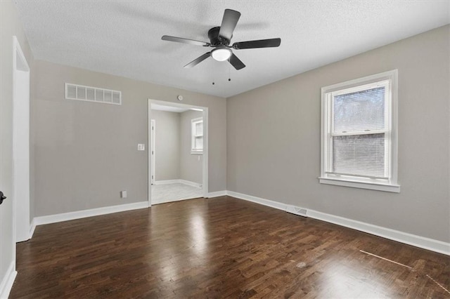 empty room with dark wood finished floors, a ceiling fan, visible vents, and baseboards