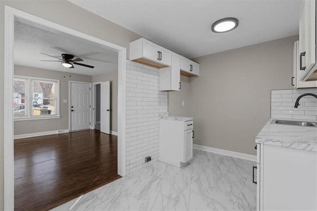 3403 Norton Ave, Kansas City, MO 64128 - kitchen featuring marble finish floor, a ceiling fan, a sink, white cabinetry, and baseboards