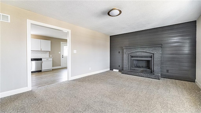 unfurnished living room with visible vents, a textured ceiling, carpet floors, baseboards, and a brick fireplace