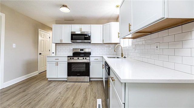 kitchen with a sink, light wood-style floors, appliances with stainless steel finishes, white cabinets, and decorative backsplash