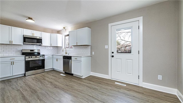 kitchen with a sink, light wood-style flooring, backsplash, and stainless steel appliances