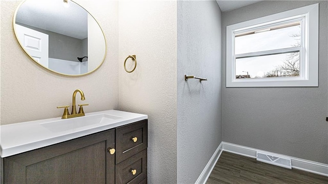 bathroom with vanity, wood finished floors, baseboards, visible vents, and a textured wall