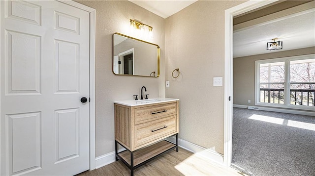 bathroom with wood finished floors, vanity, baseboards, and a textured wall