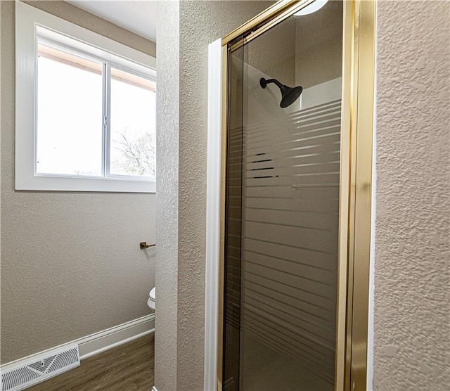 bathroom featuring visible vents, a stall shower, wood finished floors, baseboards, and a textured wall