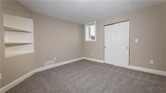 unfurnished bedroom featuring visible vents, a textured ceiling, dark carpet, a closet, and baseboards