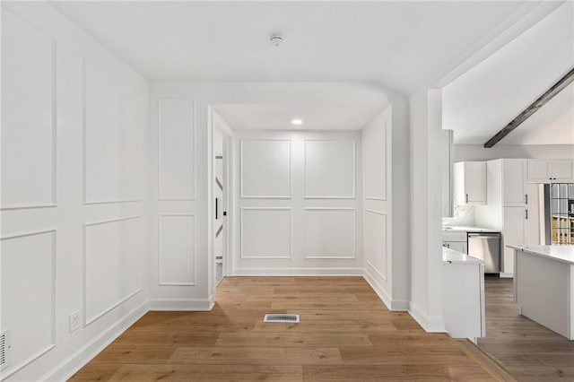 hall with a decorative wall, visible vents, and light wood-type flooring