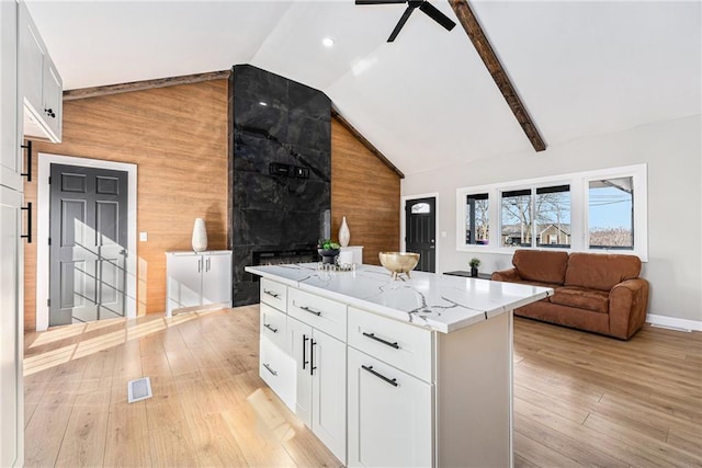 kitchen featuring light wood finished floors, visible vents, wood walls, vaulted ceiling, and light stone counters