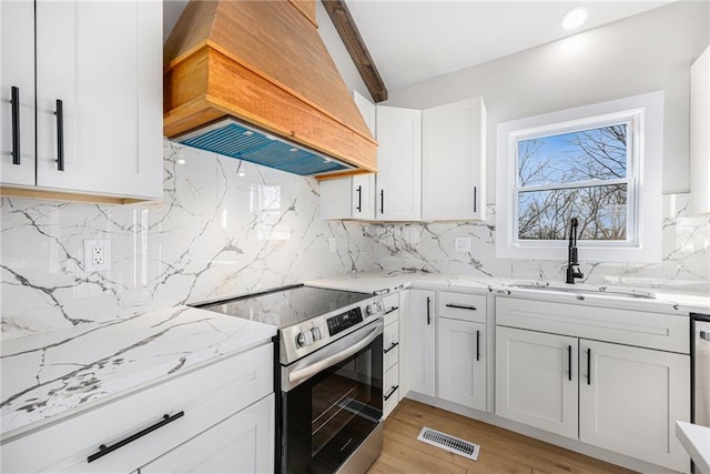 kitchen featuring light stone counters, visible vents, premium range hood, stainless steel electric stove, and a sink