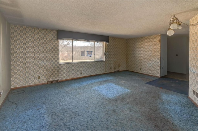 carpeted spare room with visible vents, baseboards, a textured ceiling, and wallpapered walls