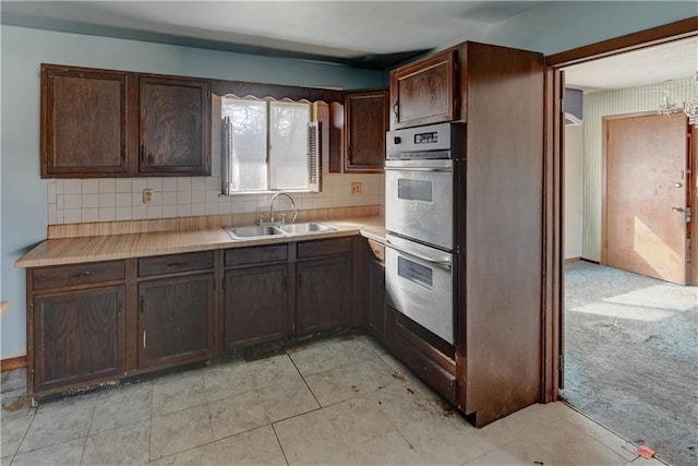 kitchen featuring dark brown cabinets, light colored carpet, light countertops, stainless steel double oven, and a sink